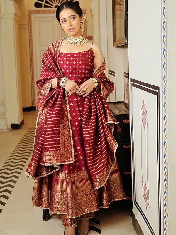 Woman wearing a cherry red self-woven vegan silk anarkali with boota and border detailing, paired with matching pants and a dupatta, ideal for a festive occasion.