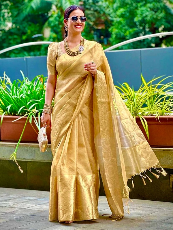 Woman in a golden saree with intricate designs, paired with traditional jewelry, showcasing festive Indian attire.