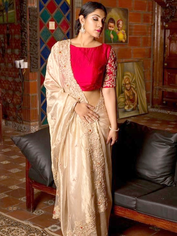 Woman wearing a red boat neck blouse with embellished sleeves and a shimmery saree with heavy embellishments on the border, ideal for a grand festive occasion.