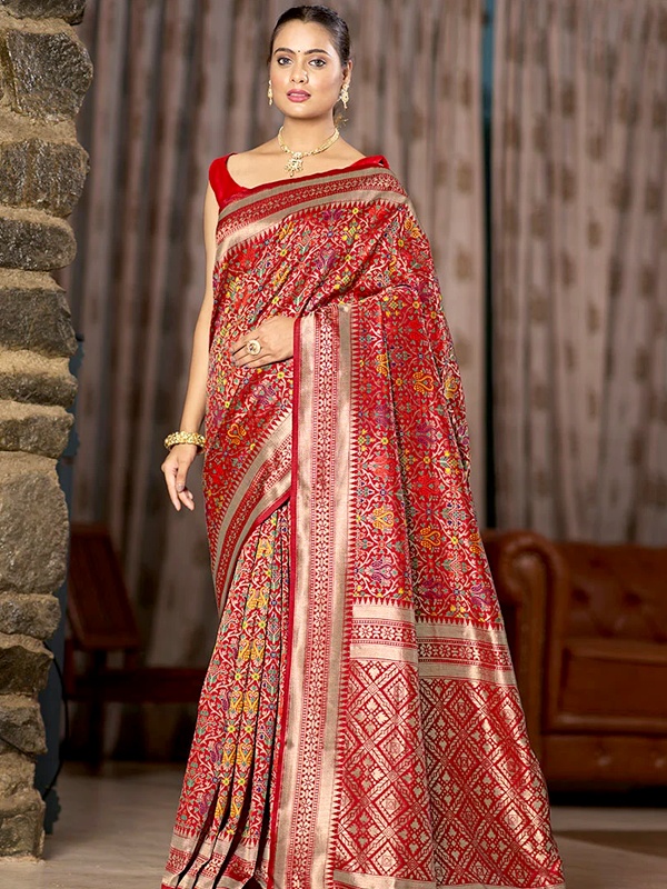 Woman adorned in a red Patola silk saree with elaborate patterns and a red blouse, complemented by traditional jewelry, ideal for festive celebrations.