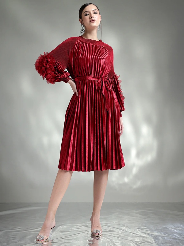 Woman wearing a knee-length red pleated dress with statement ruffled sleeves and a waist tie, paired with embellished heels.