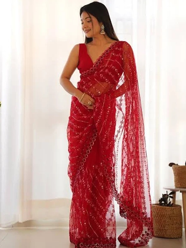 Woman wearing a red transparent net saree with sequin embellishments and a sleeveless blouse with a deep neck, ideal for a festive occasion.
