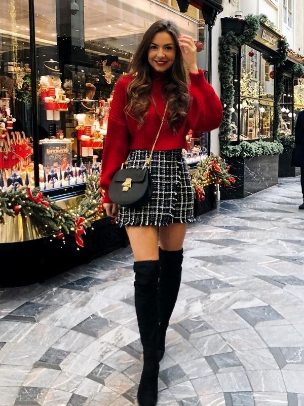 Woman in red full-sleeve sweater, checked mini skirt and black over-the-knee boots walking past festive Christmas shop displays.