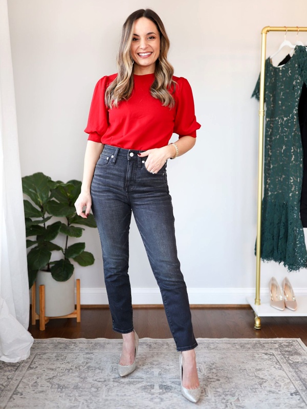 Woman wearing a red top with short sleeves and dark blue jeans, complemented by light-colored heels, showcasing a simple and stylish outfit.