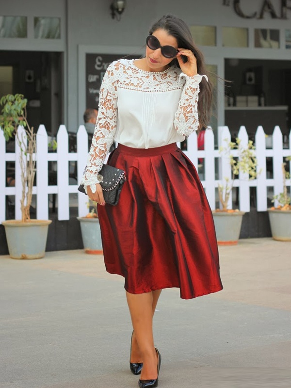 Woman wearing a white top with lace sleeves and neckline, a red knee-length pleated skirt and black heels, showcasing a stylish and festive outfit.