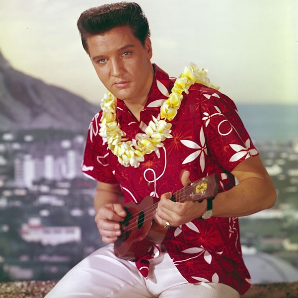 Elvis Presley wearing brightly colored Hawaiian Aloha shirts in 1961 movie Blue Hawaii popularizing tropical prints and casual resort fashion globally making island style mainstream