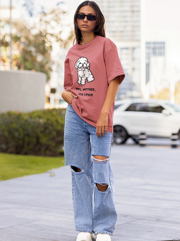Woman wearing pink dog graphic t-shirt with distressed ripped blue jeans and white sneakers in casual street style outfit
