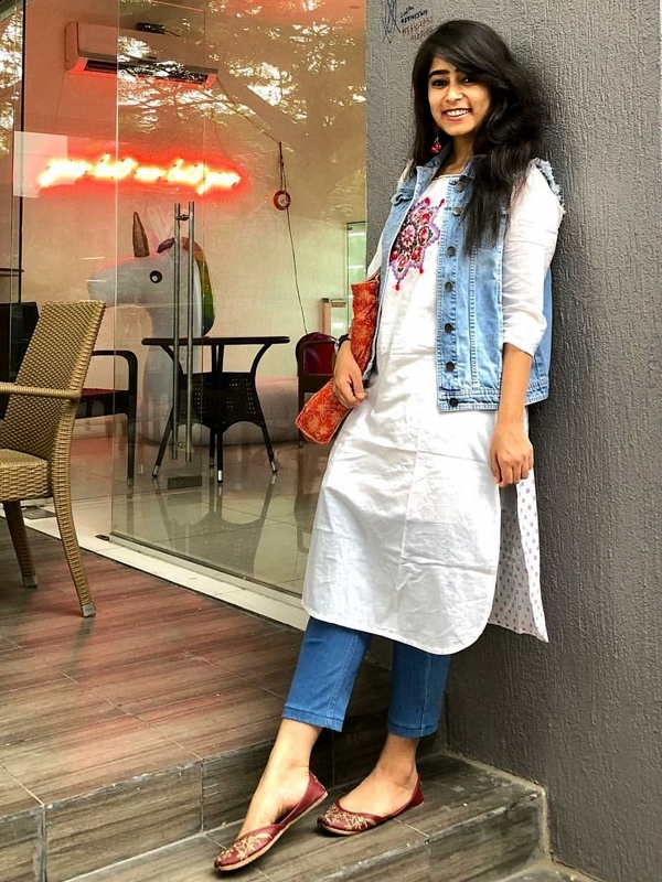 Indo-western fusion style with white kurta over blue jeans, layered denim jacket, red clutch and burgundy flats