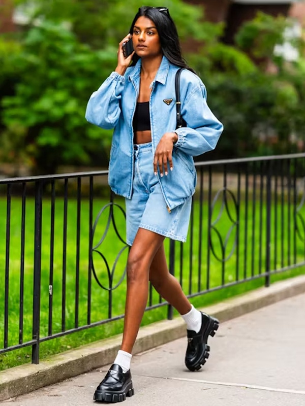 Woman in light blue denim mini jorts with oversized denim jacket - trendy double denim street style