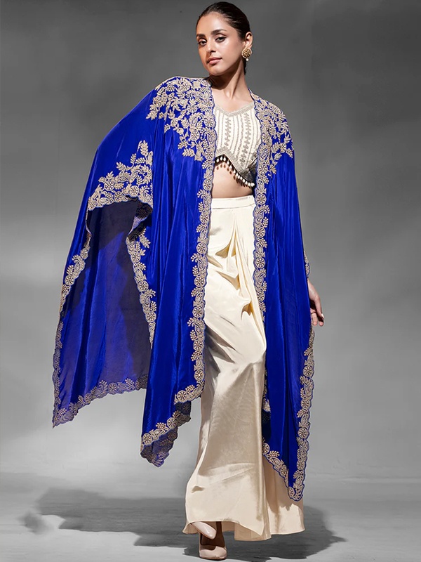 Royal blue embroidered cape jacket paired with a cream embellished crop top and smooth draped satin skirt. Royal blue embroidered cape jacket paired with a cream embellished crop top and smooth draped satin skirt.