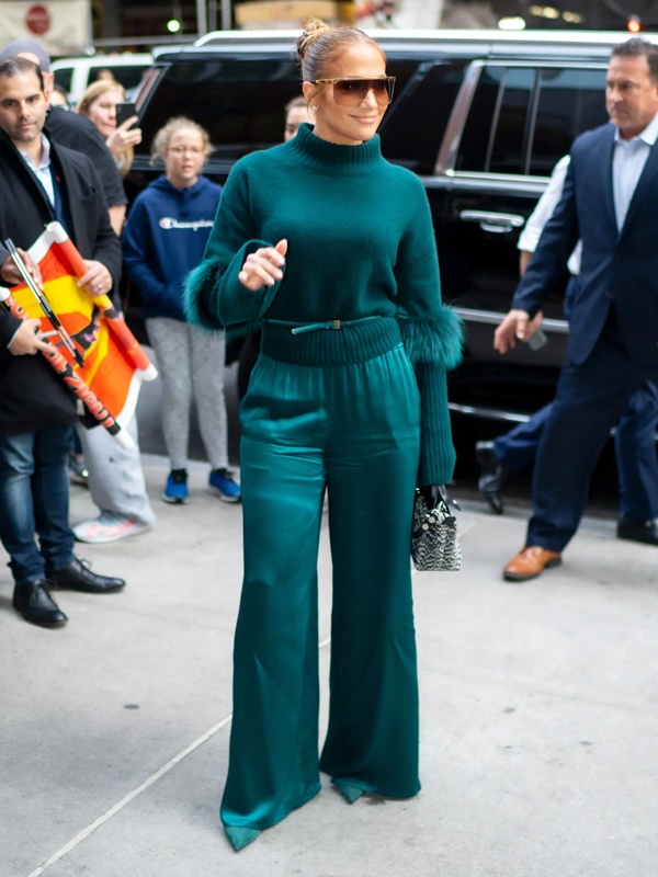 Jennifer Lopez wearing a sophisticated teal outfit, featuring a chunky knit sweater and high-waisted, wide-leg tailored trousers