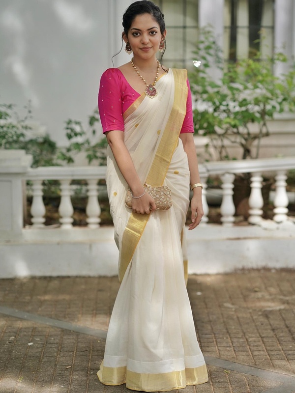 Actress Ahaana Krishna in a white saree with pink blouse and gold border, holding a gold clutch. Actress Ahaana Krishna in a white saree with pink blouse and gold border, holding a gold clutch.