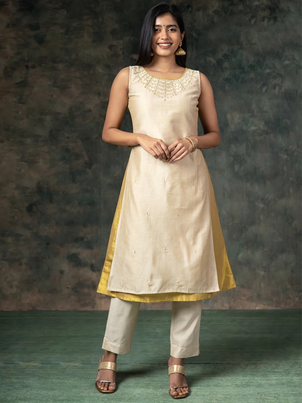 Woman wearing a cream kurta with golden embroidery and cream pants, complemented by gold sandals. Woman wearing a cream kurta with golden embroidery and cream pants, complemented by gold sandals.