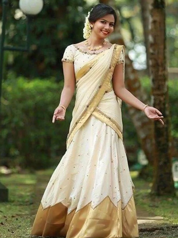 Woman adorned in a golden tissue Davani saree with a zig-zag pattern and cream base, complemented by gold jewellery. Woman adorned in a golden tissue Davani saree with a zig-zag pattern and cream base, complemented by gold jewellery.