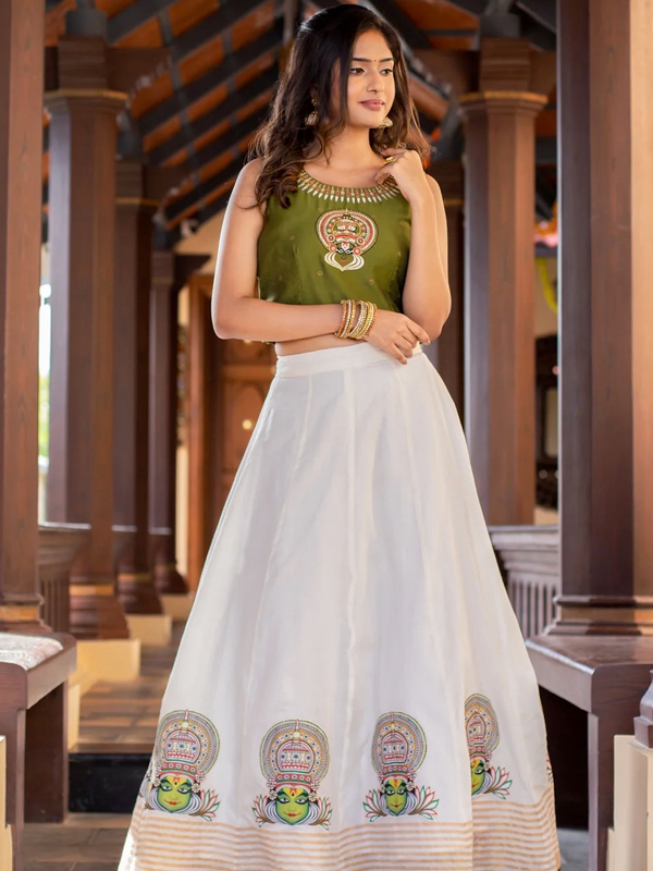 Woman wearing a green crop top with an off-white skirt, both featuring Kathakali embroidery, complemented by gold jewellery. Woman wearing a green crop top with an off-white skirt, both featuring Kathakali embroidery, complemented by gold jewellery.