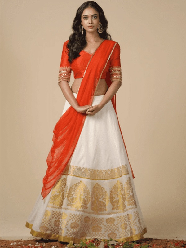 Woman in an ivory handloom skirt with gold accents, complemented by an orange blouse and dupatta, showcasing traditional fashion. Woman in an ivory handloom skirt with gold accents, complemented by an orange blouse and dupatta, showcasing traditional fashion.