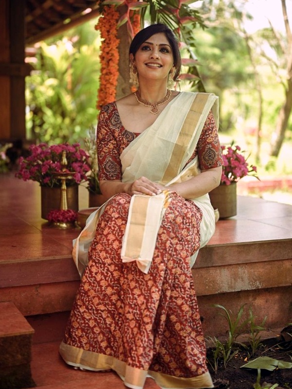 Woman in a cream Kalamkari print Kerala saree with red and gold patterns, sitting gracefully in a festive setting. Woman in a cream Kalamkari print Kerala saree with red and gold patterns, sitting gracefully in a festive setting.