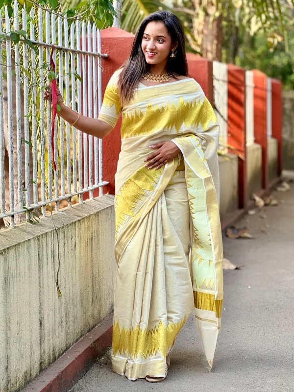 Woman in a golden Kerala tissue saree with cream and gold accents, showcasing regional design. Woman in a golden Kerala tissue saree with cream and gold accents, showcasing regional design.