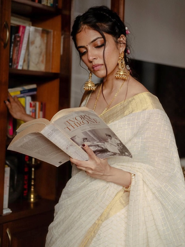 Actress Malavika Mohanan reading a book, wearing a cream Kasavu saree with golden checks and gold jewellery. Actress Malavika Mohanan reading a book, wearing a cream Kasavu saree with golden checks and gold jewellery.