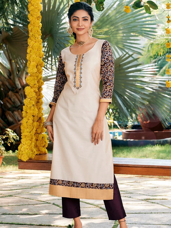 Woman in an off-white kurta with floral embroidery and Kalamkari sleeves, standing outdoors near a flower arrangement. Woman in an off-white kurta with floral embroidery and Kalamkari sleeves, standing outdoors near a flower arrangement.