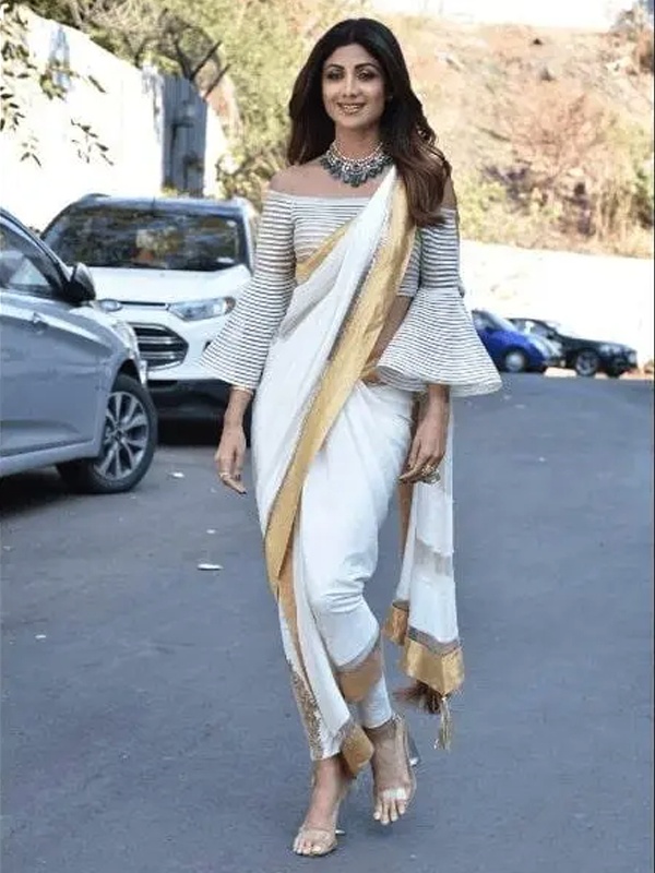 Actress Shilpa Shetty in a striped off-shoulder top with a white saree, showcasing a fusion of Indian and western fashion. Actress Shilpa Shetty in a striped off-shoulder top with a white saree, showcasing a fusion of Indian and western fashion.