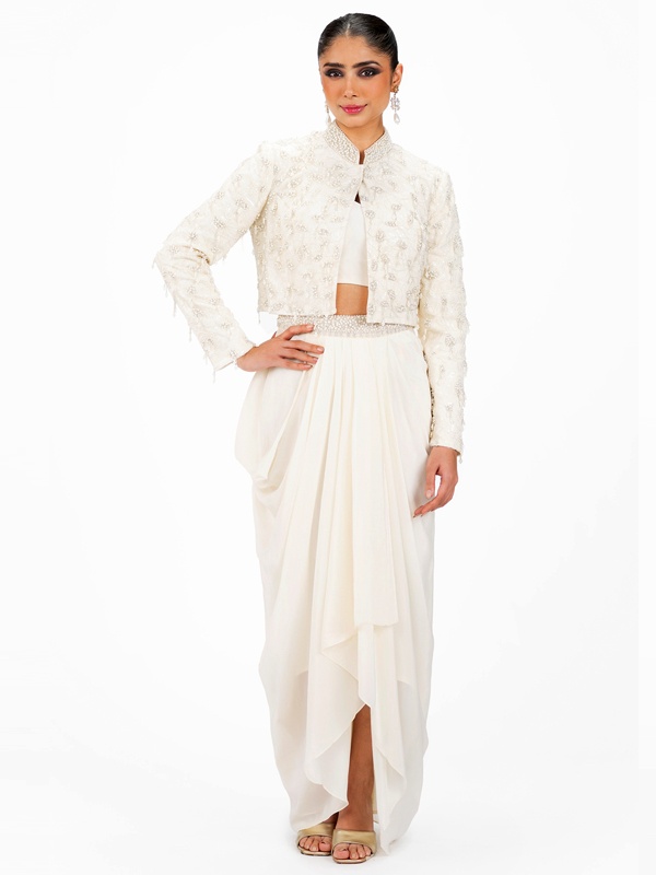 Woman in a white co-ord set with a draped skirt and embroidered jacket, showcasing detailed needlework. Woman in a white co-ord set with a draped skirt and embroidered jacket, showcasing detailed needlework.