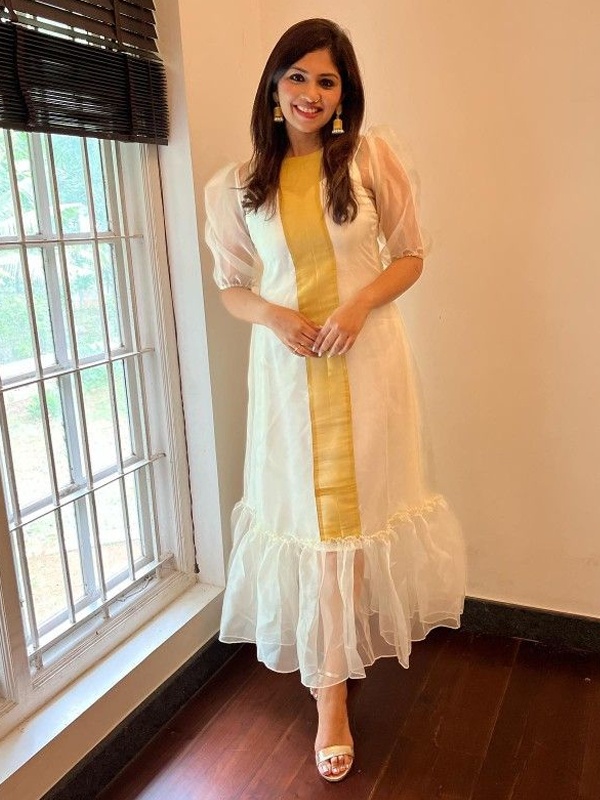 Woman wearing a yellow and white kurta with ruffled hem and white pants, complemented by gold earrings and sandals. Woman wearing a yellow and white kurta with ruffled hem and white pants, complemented by gold earrings and sandals.