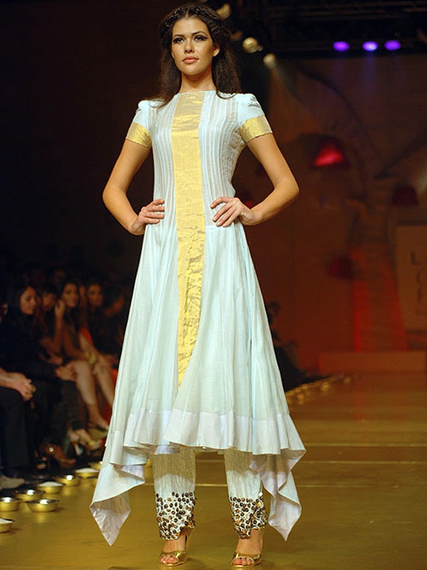 Model on runway showcasing a white kurta with gold accents and white pants with gold hem design. Model on runway showcasing a white kurta with gold accents and white pants with gold hem design.