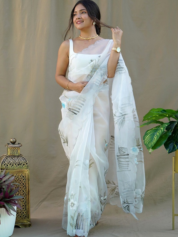 Woman in a white organza saree with floral embroidery, accessorized with a gold necklace and watch. Woman in a white organza saree with floral embroidery, accessorized with a gold necklace and watch.
