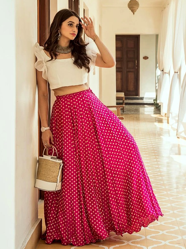 Woman wearing a white organza ruffle top and a pink polka dot skirt, accessorized with a statement necklace and a stylish handbag. Woman wearing a white organza ruffle top and a pink polka dot skirt, accessorized with a statement necklace and a stylish handbag.