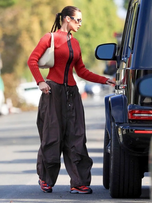Bella Hadid in bold red high-neck top with voluminous dark grey parachute trousers, white shoulder bag and matching red sneakers for statement street style
