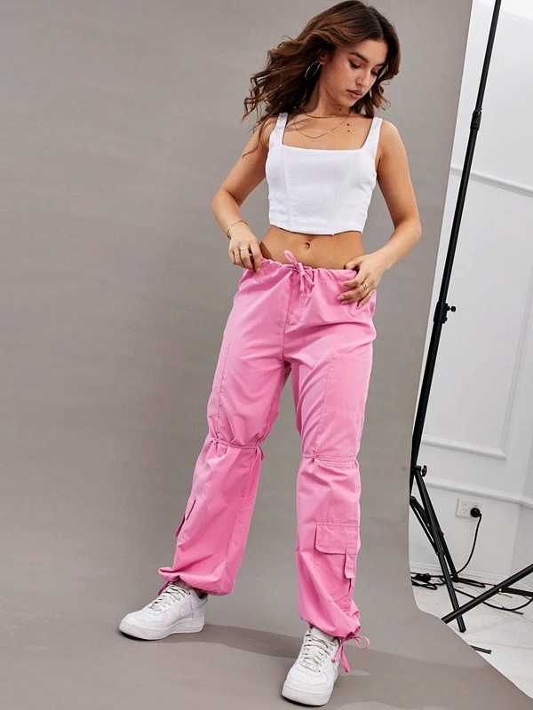 Bold color contrast outfit with white cropped top and bright pink cargo parachute pants accessorized with gold necklace and white sneakers for college