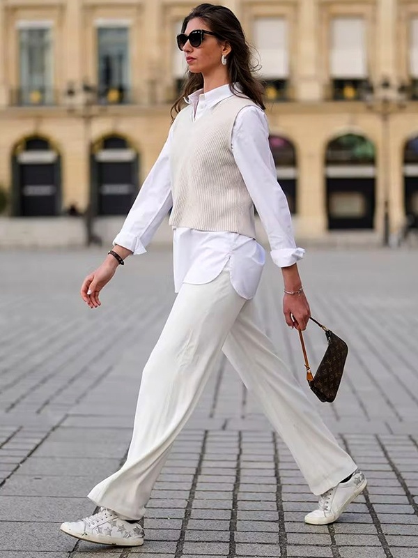 Monochrome all-white street style outfit crisp white shirt under off-white sleeveless sweater vest with matching cream pants white leather sneakers and structured ivory handbag