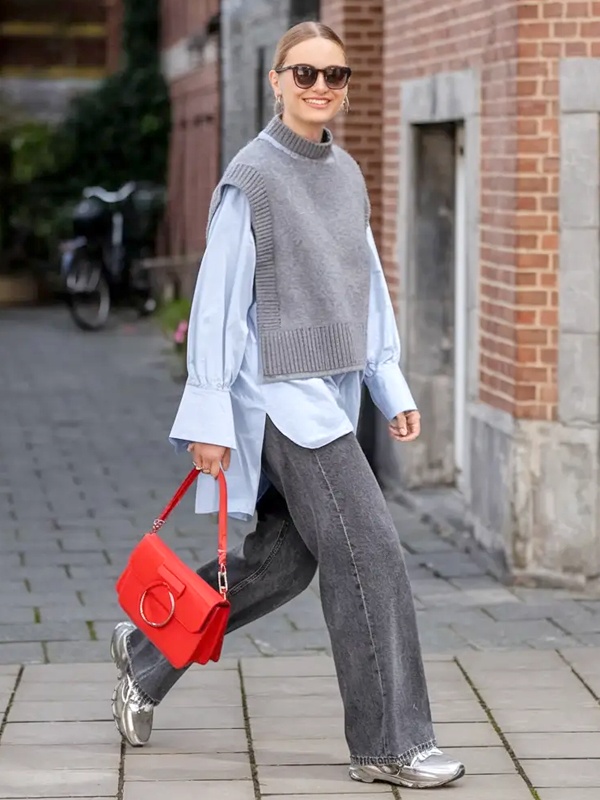 Neutral outfit grey sleeveless knit vest over powder blue collared shirt with charcoal grey denim silver metallic flats and vibrant red leather handbag accent