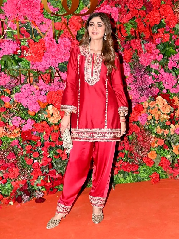 Shilpa Shetty wearing deep red silk Chanderi short kurta with Dogri salwar, silk organza dupatta, three-quarter bell sleeves, kirandori and sitaara embroidery, Banarasi kinari border, standing against floral backdrop