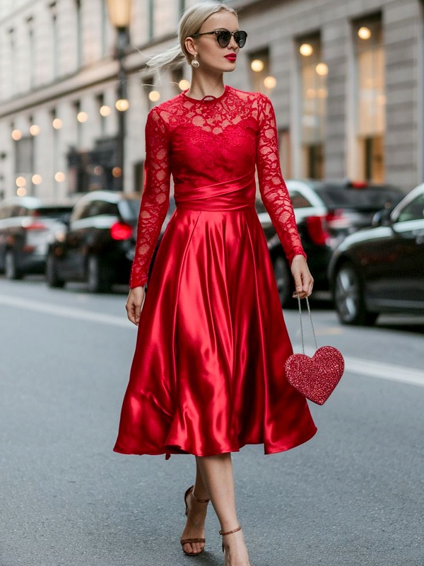 Woman wearing red Valentine's Day dress with sheer floral lace long-sleeve bodice, high neckline, satin A-line skirt, nude strappy heels and red glitter heart-shaped handbag